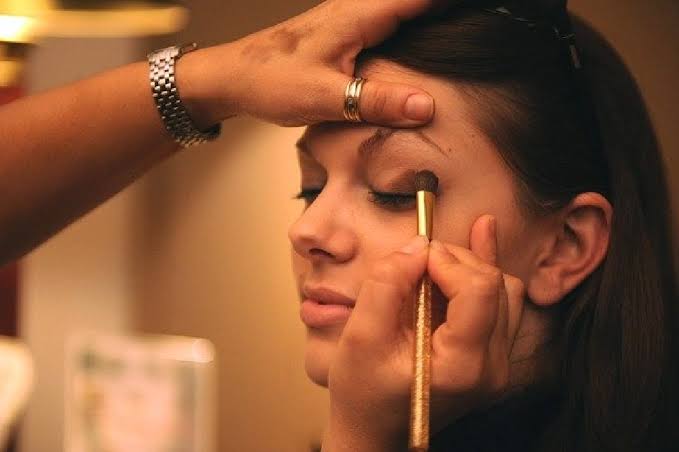 Professional makeup artist applying eye makeup to a woman using a makeup brush.